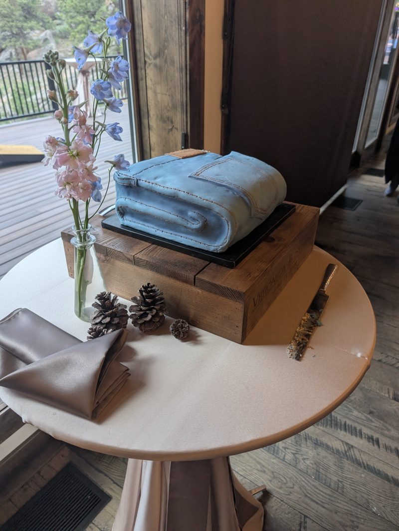 The folded-jeans cake on a wooden crate beside wildflowers and pine cones